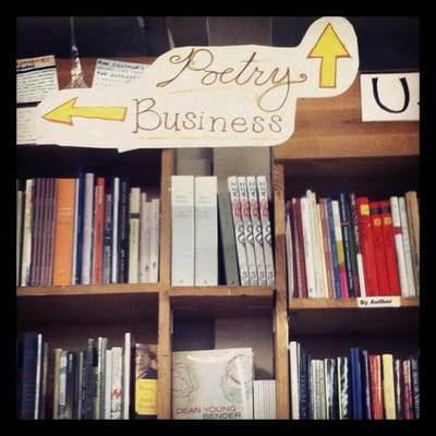 A photo of bookshelves inside Green Apple Books. A sign on top reads "Poetry" and "Business," and has the arrows pointing in different directions.