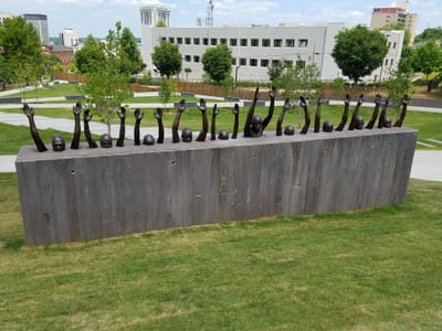 A sculpture made of a cement rectangle, with human figures in bronze emerging from the top with arms raised.