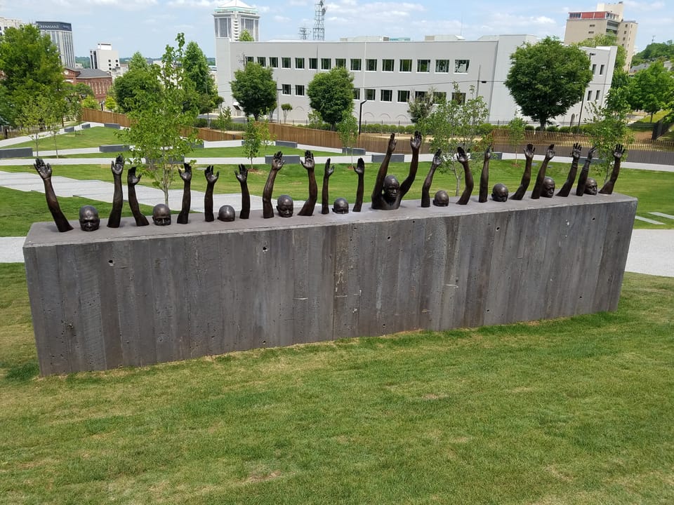 A sculpture made of a cement rectangle, with human figures in bronze emerging from the top with arms raised.
